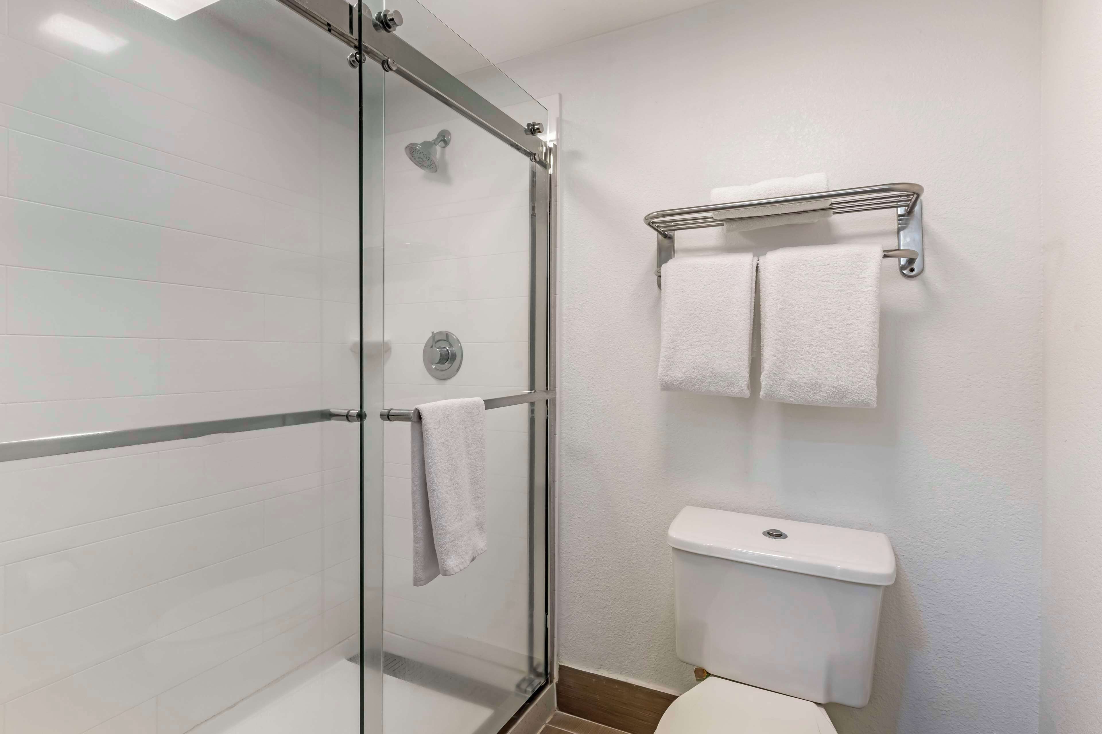 Uma casa de banho moderna com chuveiro envidraçado, sanita e um porta-toalhas com duas toalhas.