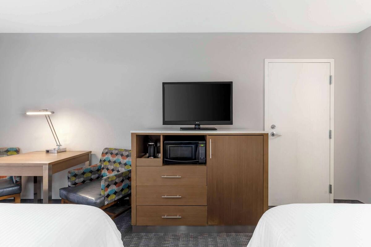 A hotel room with a bed, a desk with a lamp, a TV, a microwave, and a wardrobe.