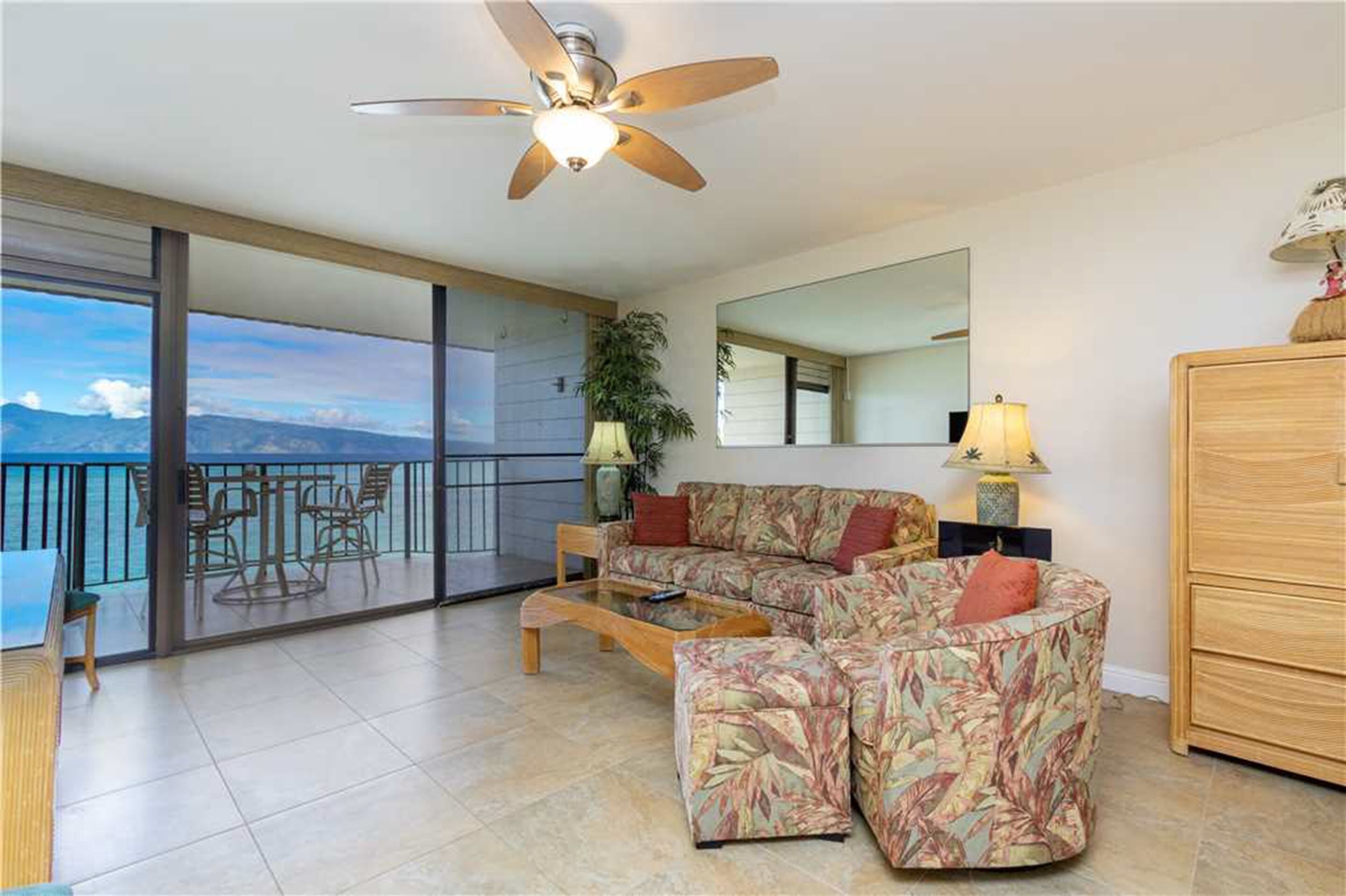A spacious living room with a large window, a ceiling fan, a sofa set, a coffee table, and a wooden cabinet.