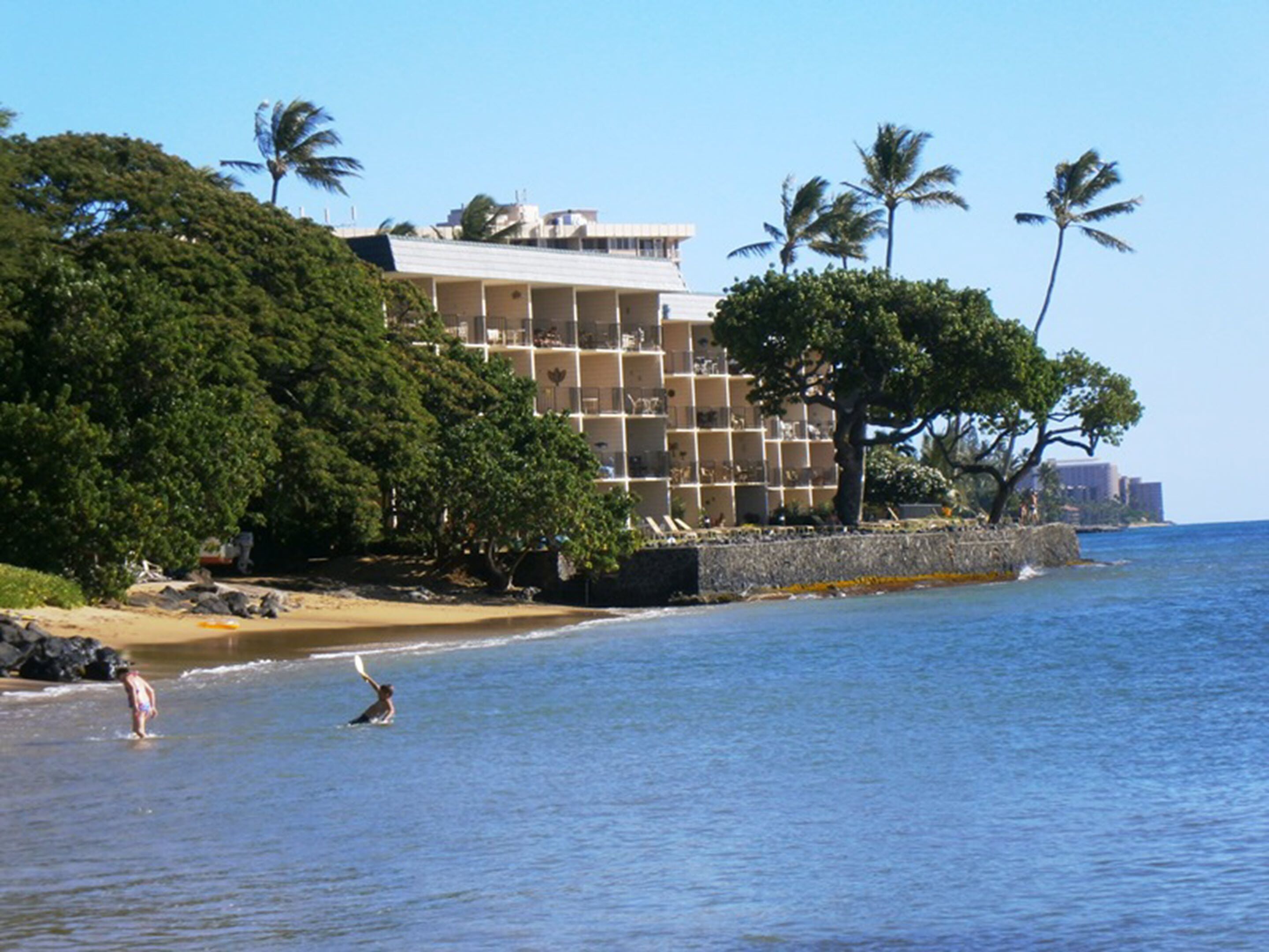 A beachfront hotel with multiple balconies, palm trees, and a sandy beach.