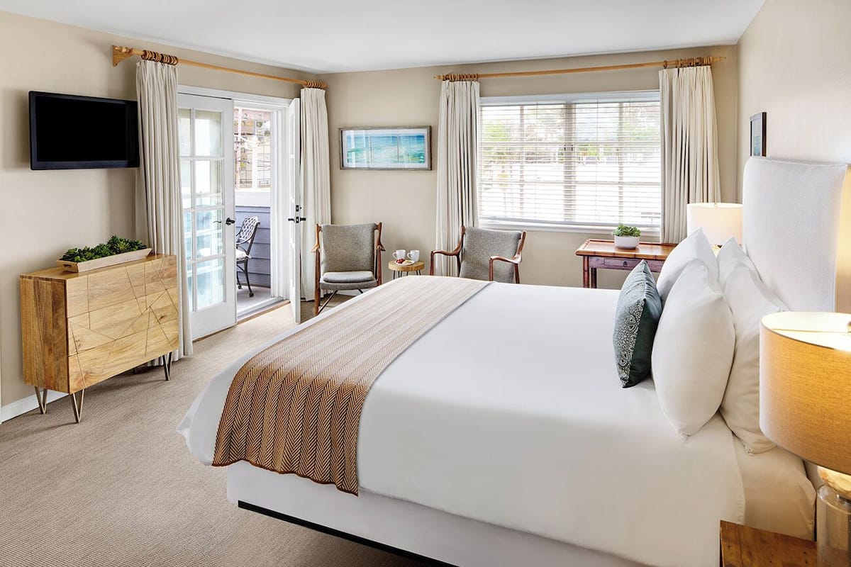 A hotel room with a large bed, a TV mounted on the wall, a desk with a chair, and a window with curtains.