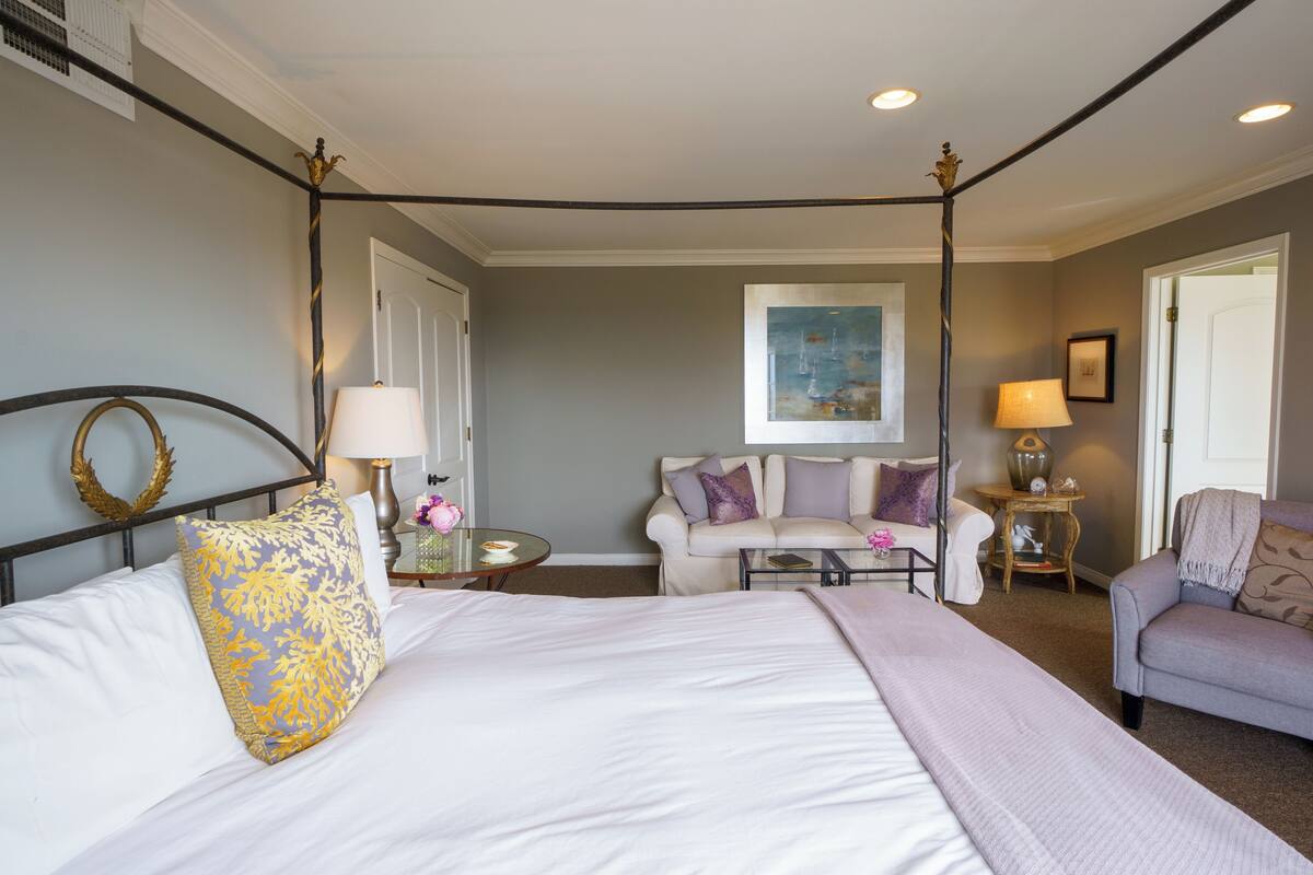 A bedroom with a four-poster bed, a sofa, a small table, and a lamp.