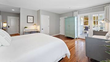 A bedroom with a large bed, a desk with a lamp, a wardrobe, and a view through a glass door.