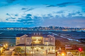 A two-story building with a balcony, located near a coastline with a view of the ocean and city lights in the background.