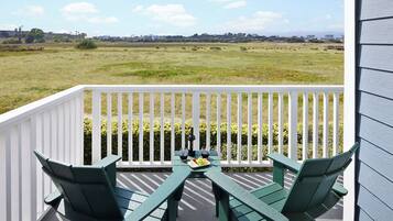 A balcony with a white railing, two green Adirondack chairs, and a table with a plate of food and a bottle of wine.
