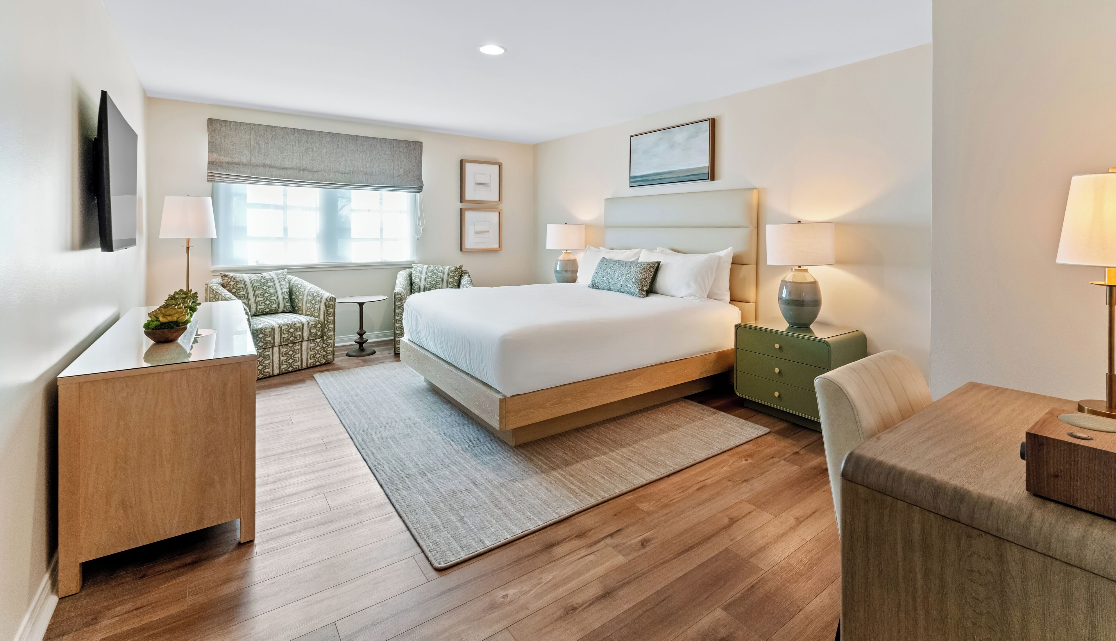 A modern hotel room with a large bed, two bedside tables with lamps, a small sofa, and a desk.