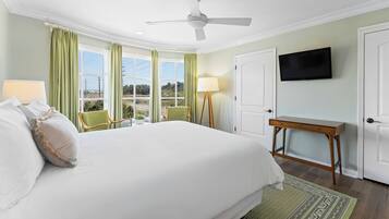 A hotel room with a large bed, a ceiling fan, a TV, a desk, and a view of the outdoors.