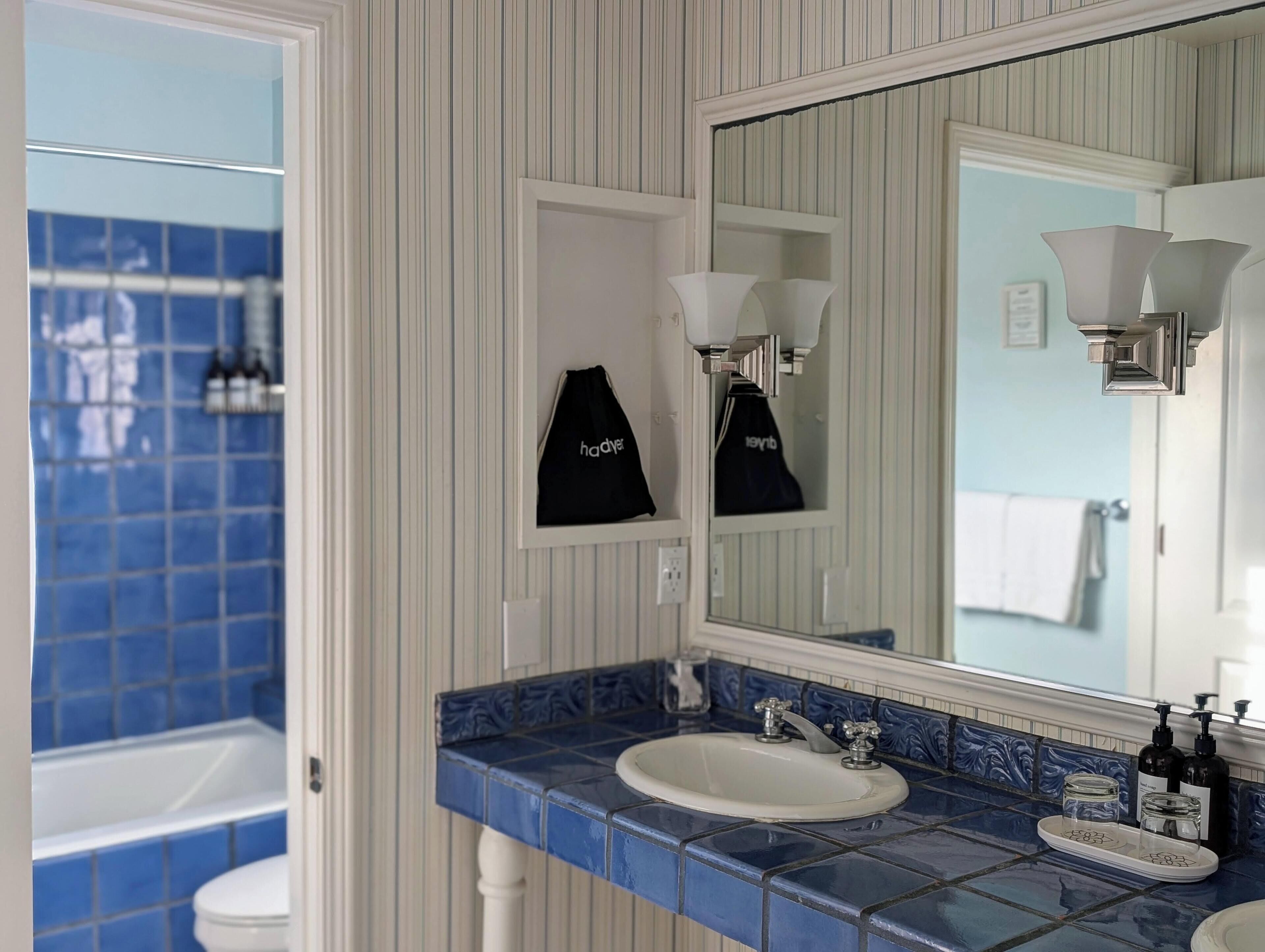 Un bagno con un lavandino rivestito di piastrelle blu, uno specchio e due asciugamani neri appesi a ganci.