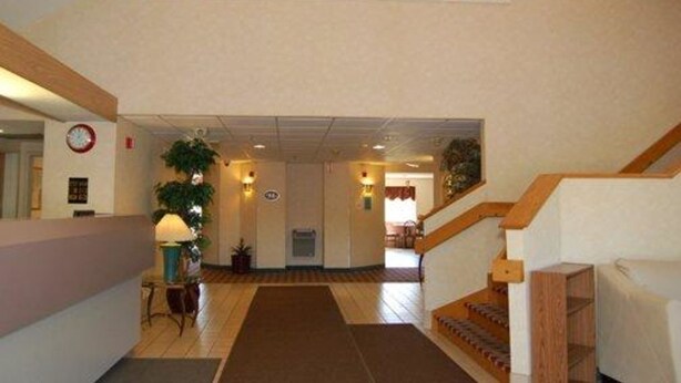 A hotel lobby with a staircase, a reception desk, a clock, and a plant. - Rodeway Inn Willington North (Willington)
