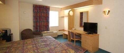 A hotel room with a large bed, a desk with a chair, a television, and a window with curtains.