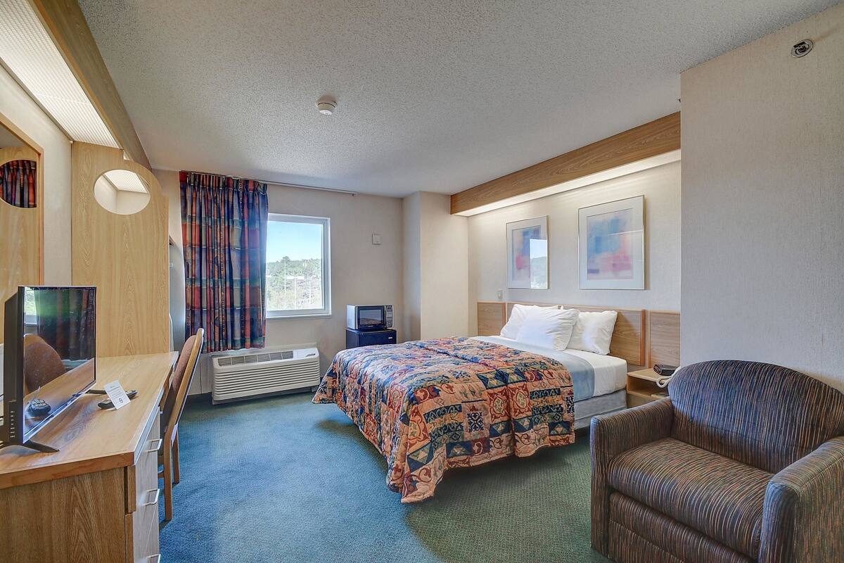A hotel room with a bed, a desk with a computer, a chair, a TV, and a window with curtains.