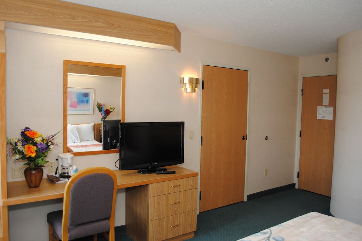 A hotel room with a wooden desk, a television, a chair, a bed, and a door.