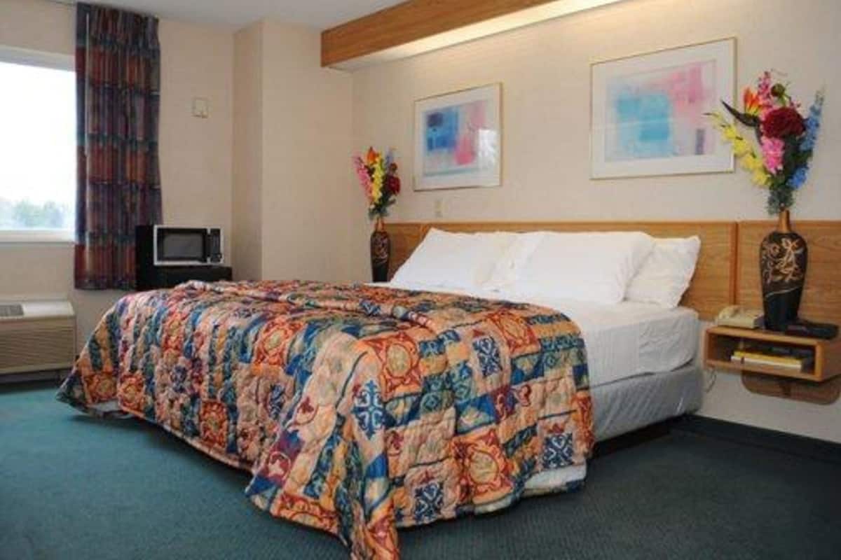 A hotel room with a large bed, a wooden headboard, two paintings on the wall, and a nightstand with a vase of flowers.