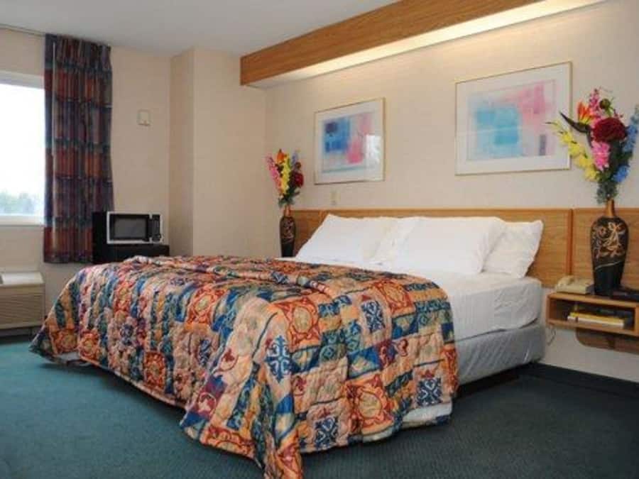 A hotel room with a large bed, a wooden headboard, two paintings on the wall, and a nightstand with a vase of flowers.