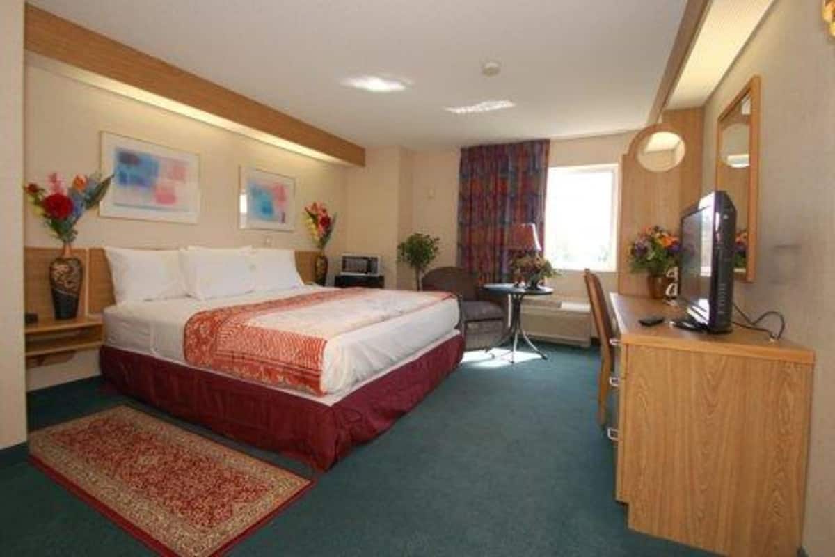 A hotel room with a bed, a desk, a chair, a computer, and a TV.
