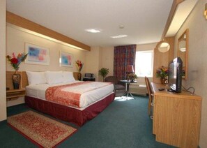 A hotel room with a bed, a desk, a chair, a computer, and a TV.