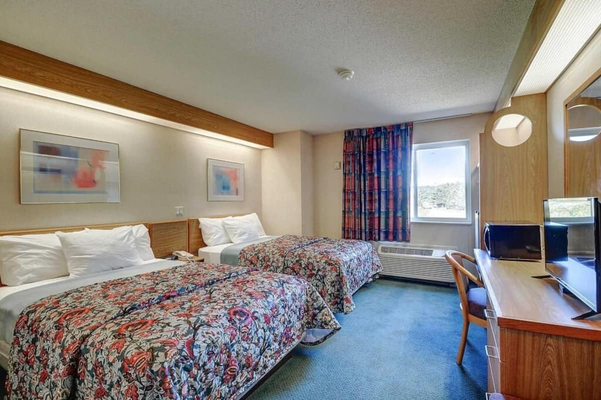 A hotel room with two beds, a desk, a chair, a television, and a window with curtains.
