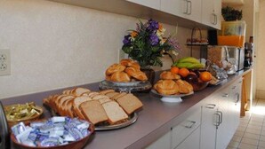 A buffet with various food items including bread, pastries, fruits, and a flower arrangement. - Rodeway Inn Willington North (Willington)