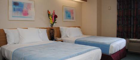 A hotel room with two beds, a vase with flowers, and two framed abstract paintings on the wall.
