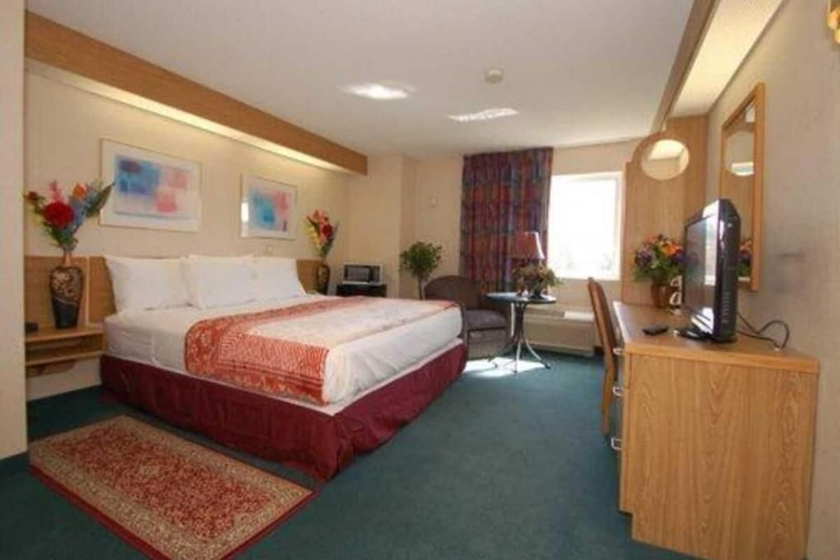 A hotel room with a bed, a desk, a television, a chair, a small table, and a window with curtains.
