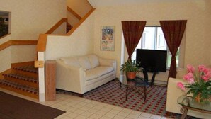 A living room with a sofa, a coffee table, a TV, a staircase, and a window with curtains. - Rodeway Inn Willington North (Willington)