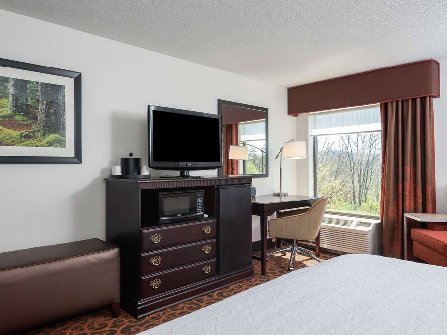 A hotel room with a bed, a desk with a computer, a television, a microwave, and a seating area.