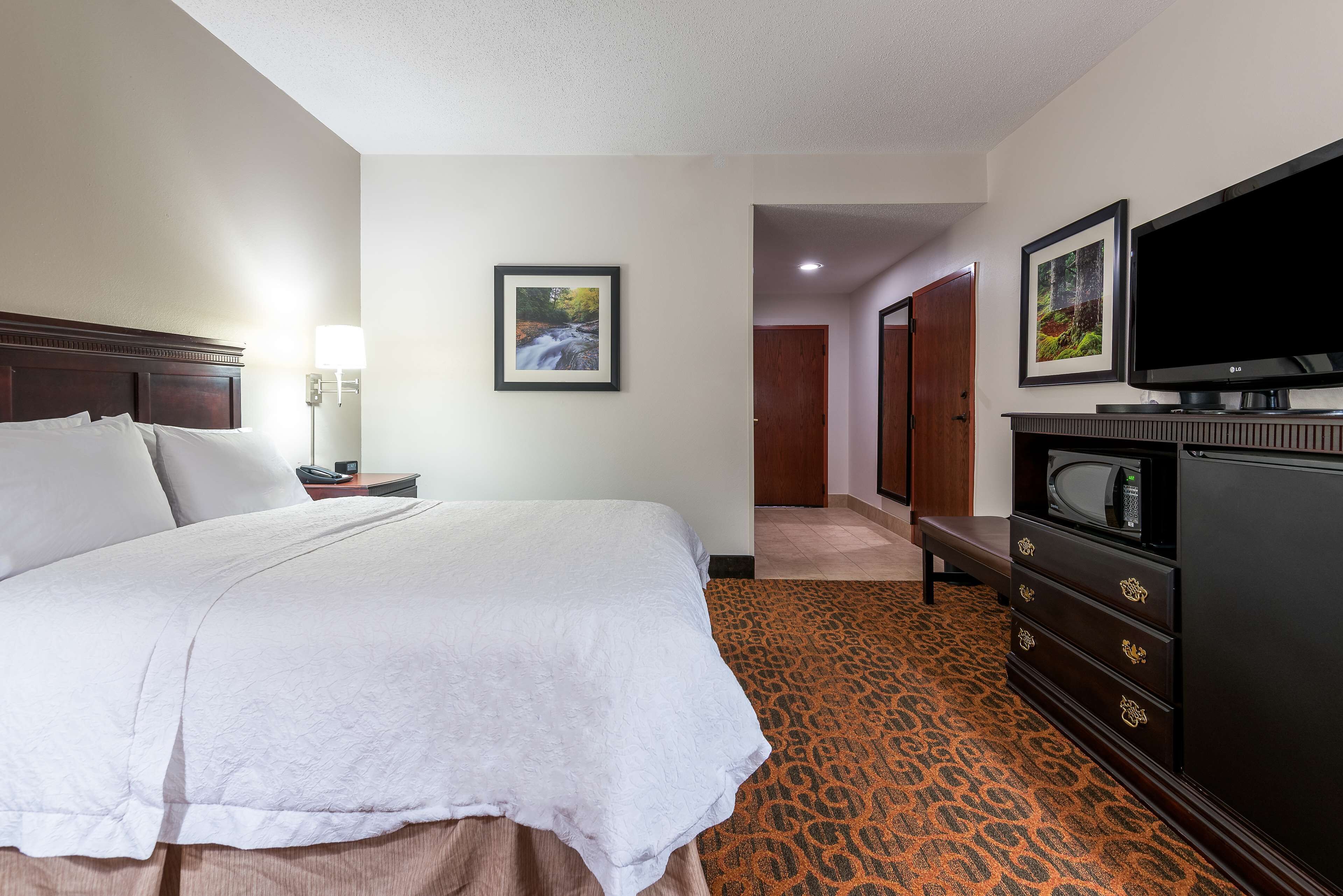 A hotel room with a bed, a dresser, a television, and framed pictures on the wall.