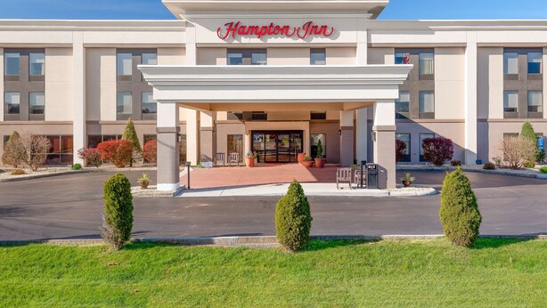Ein Hampton Inn Hotel mit moderner Fassade, einem überdachten Eingang und einer begrünten Auffahrt.