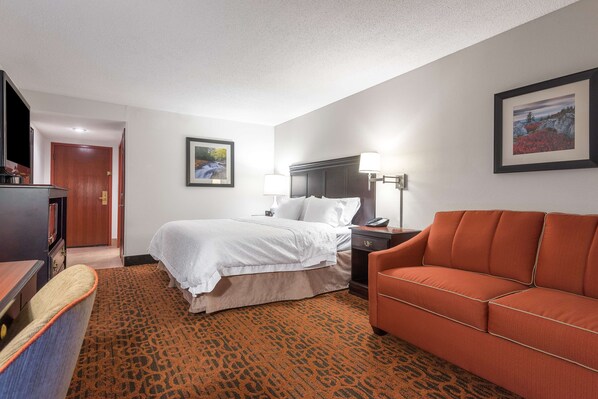 Une chambre d’hôtel avec un lit, un canapé, un bureau, une lampe et un tableau encadré au mur.