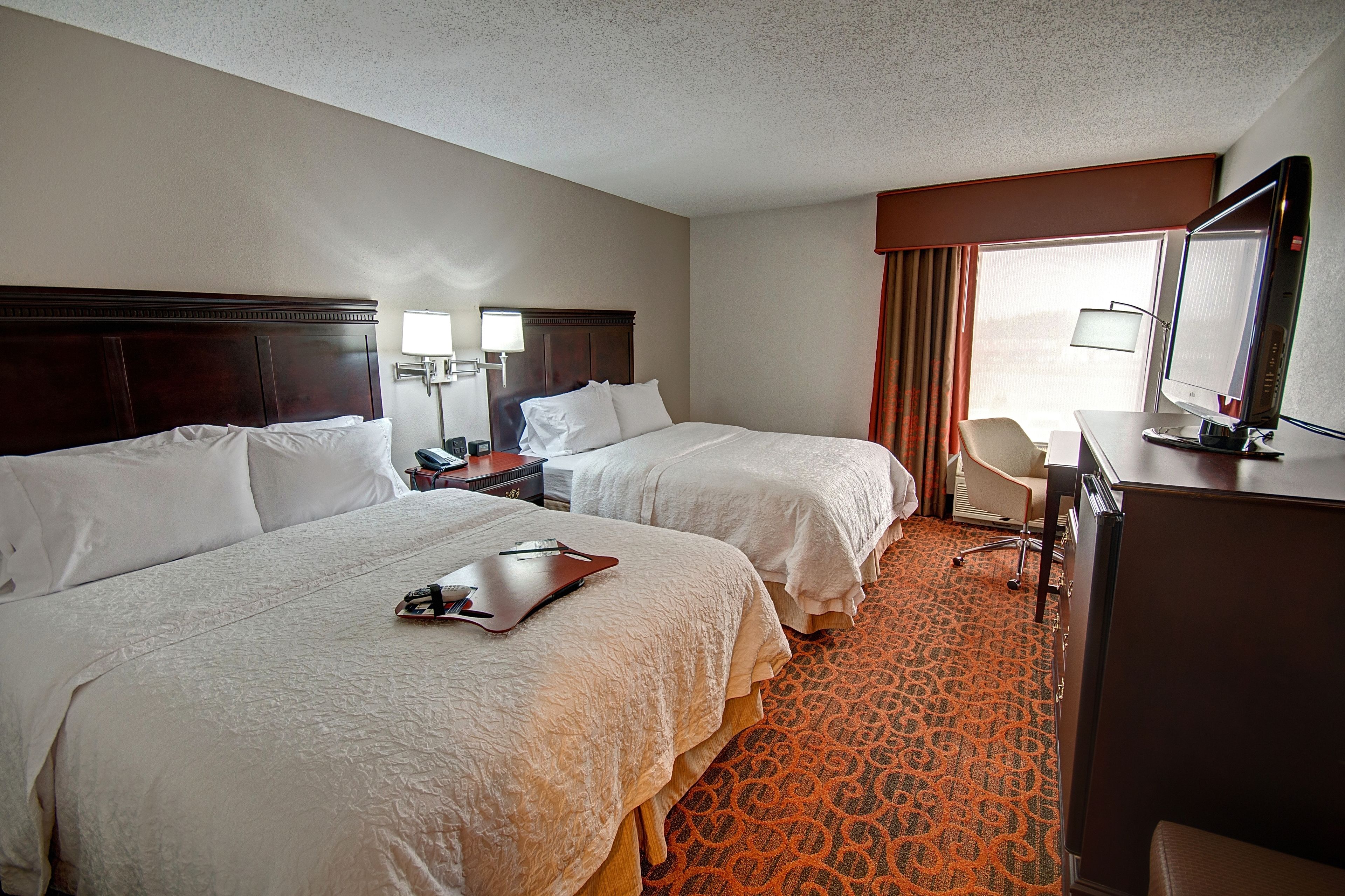 A hotel room with two beds, a desk, a chair, and a TV.