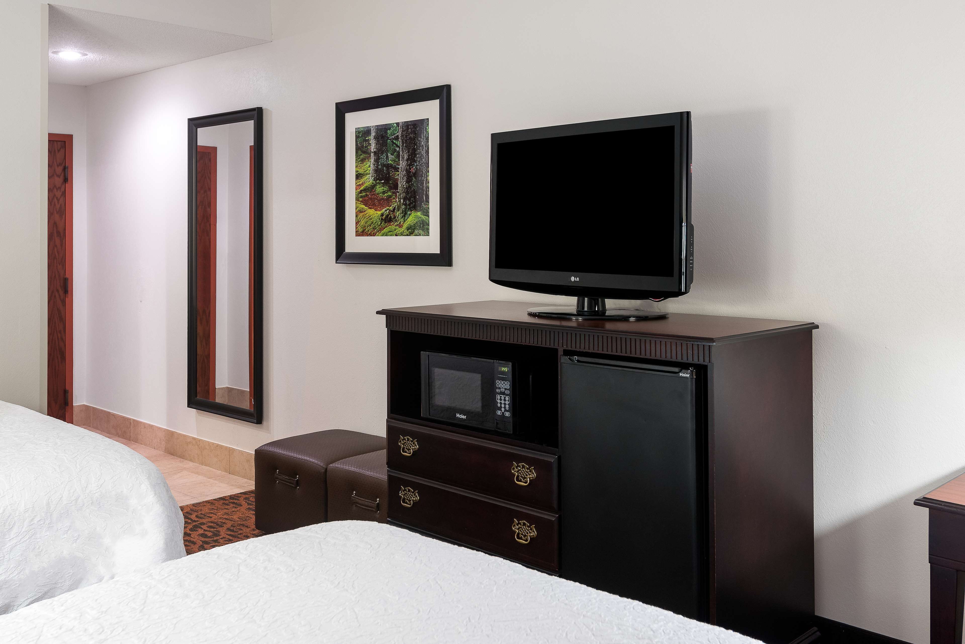 A hotel room with a bed, a TV on a cabinet, a microwave, and a refrigerator.