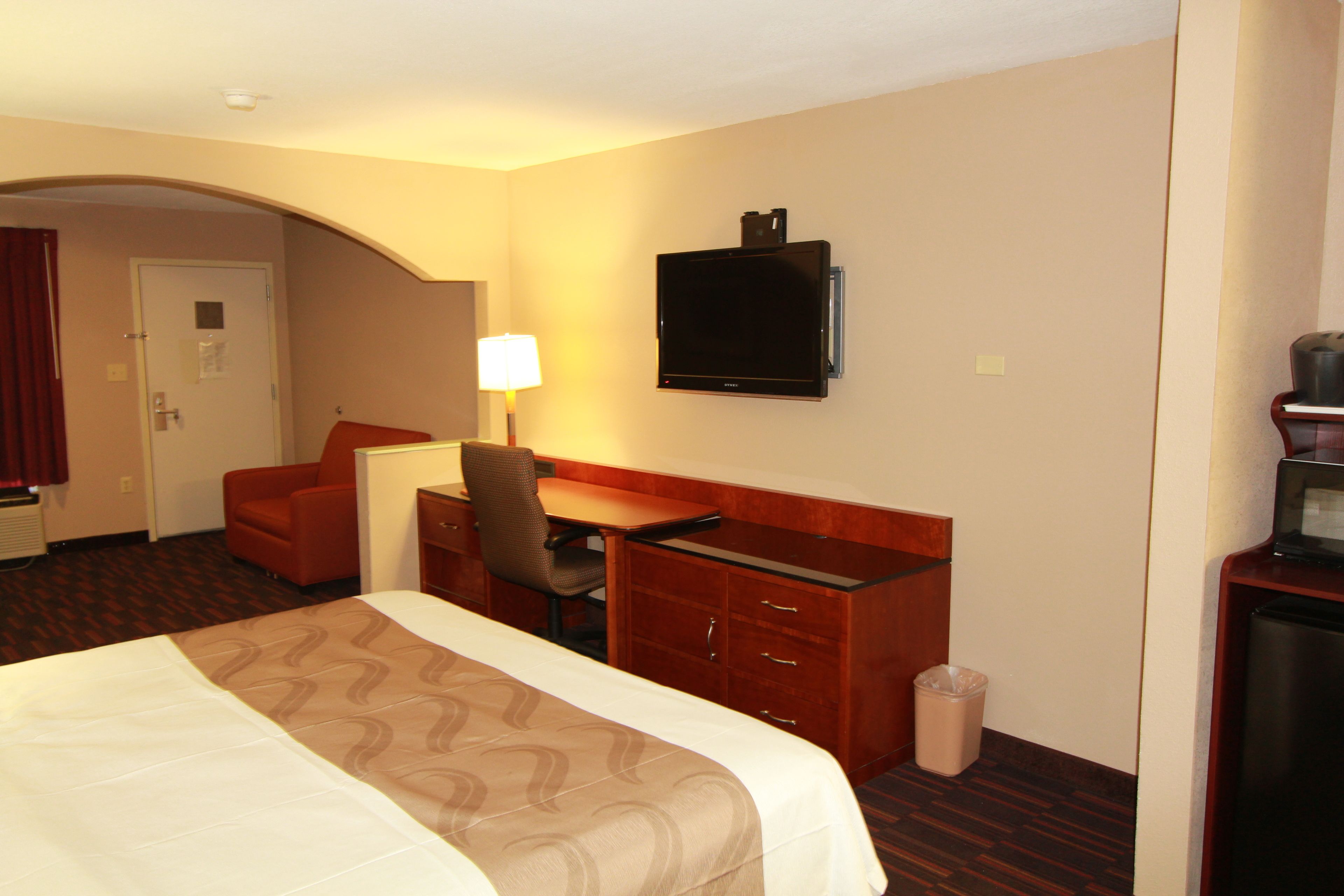Habitación de hotel con cama, escritorio, silla, televisor y basurero.