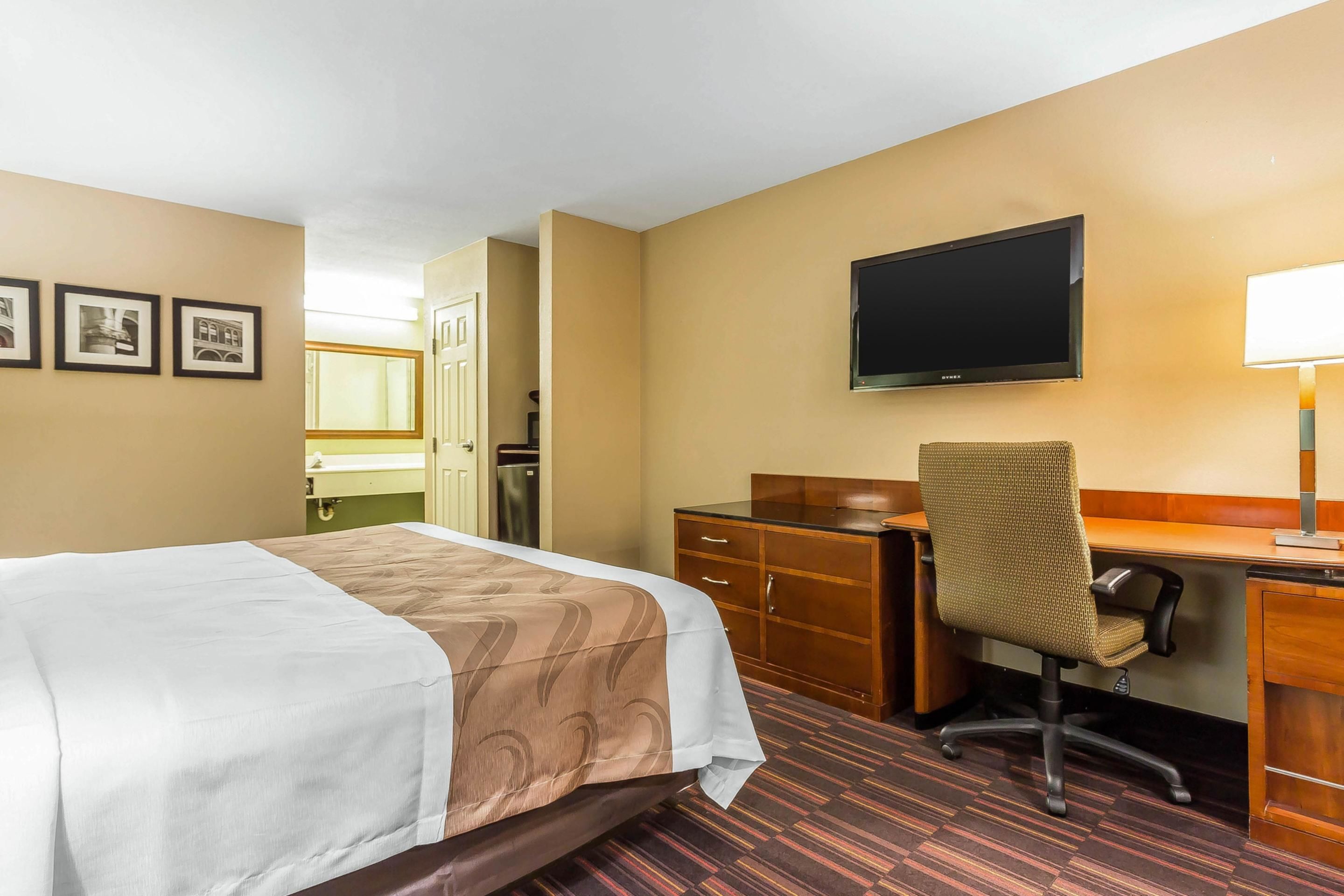 A hotel room with a bed, desk, chair, television, and a door leading to a bathroom.