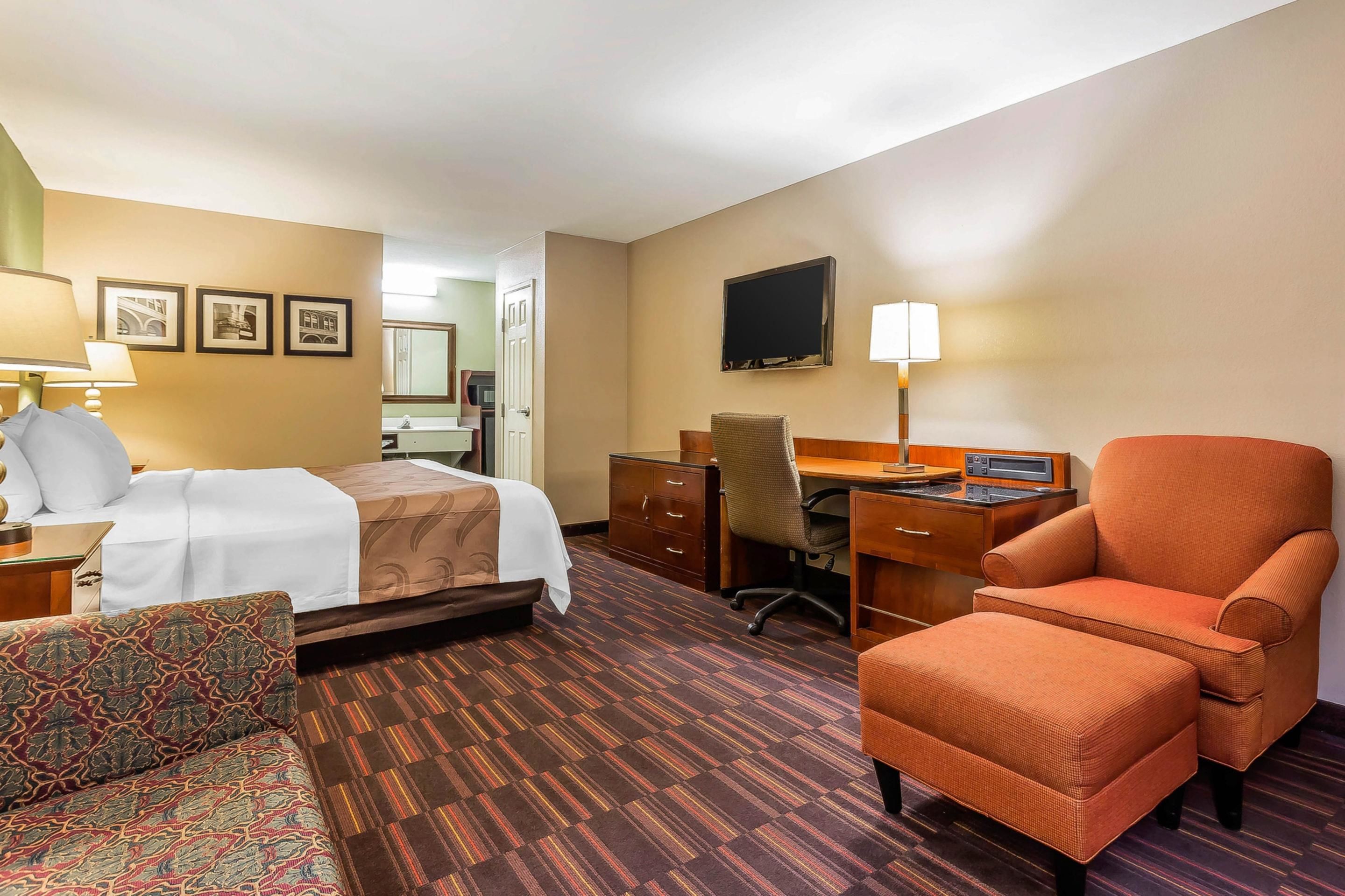 A hotel room with a bed, a desk, a chair, a sofa, and a TV.