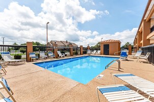 Una piscina con sillas de descanso y una valla, rodeada de edificios.