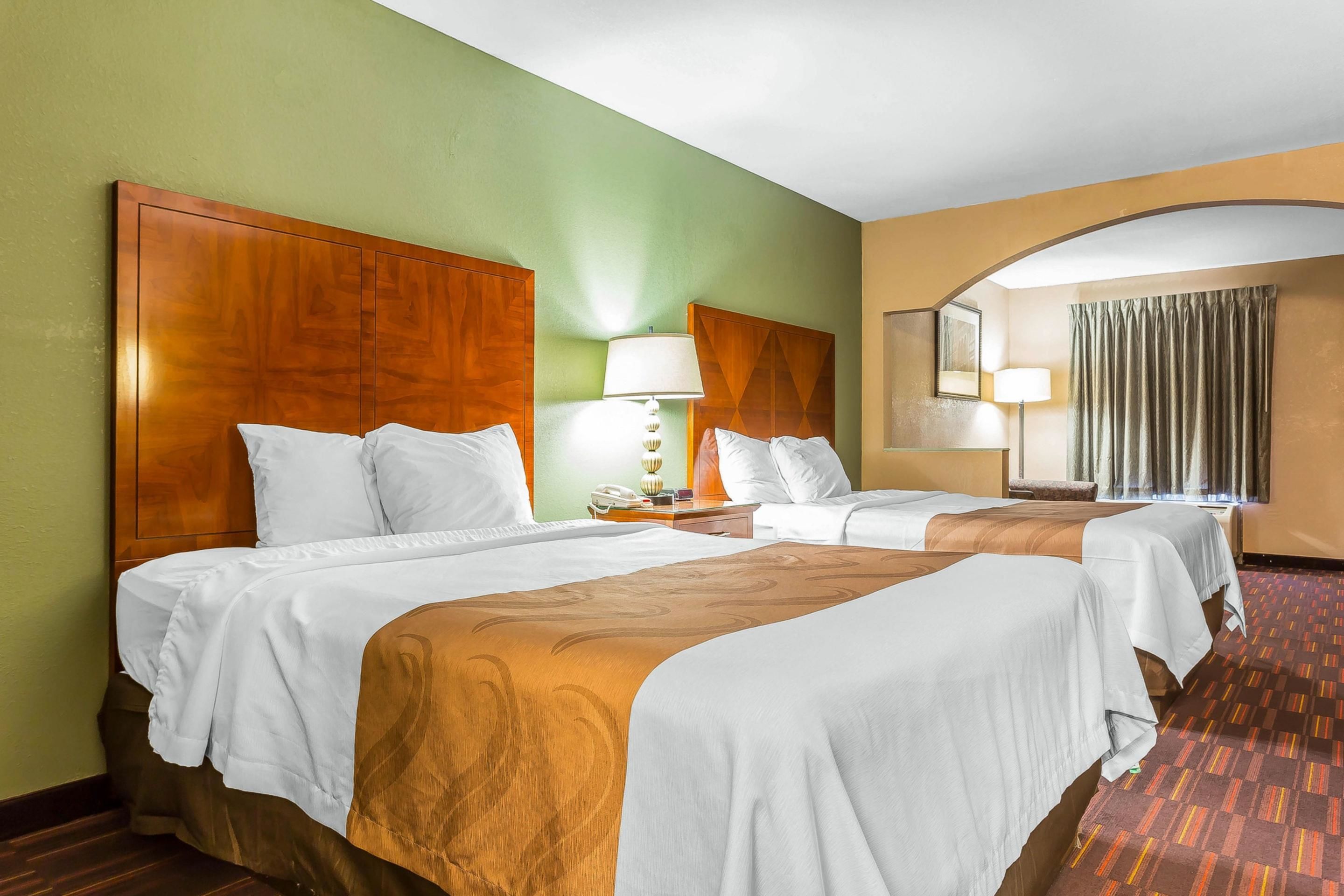 A hotel room with two beds, a wooden headboard, a nightstand with a lamp, and a large mirror.