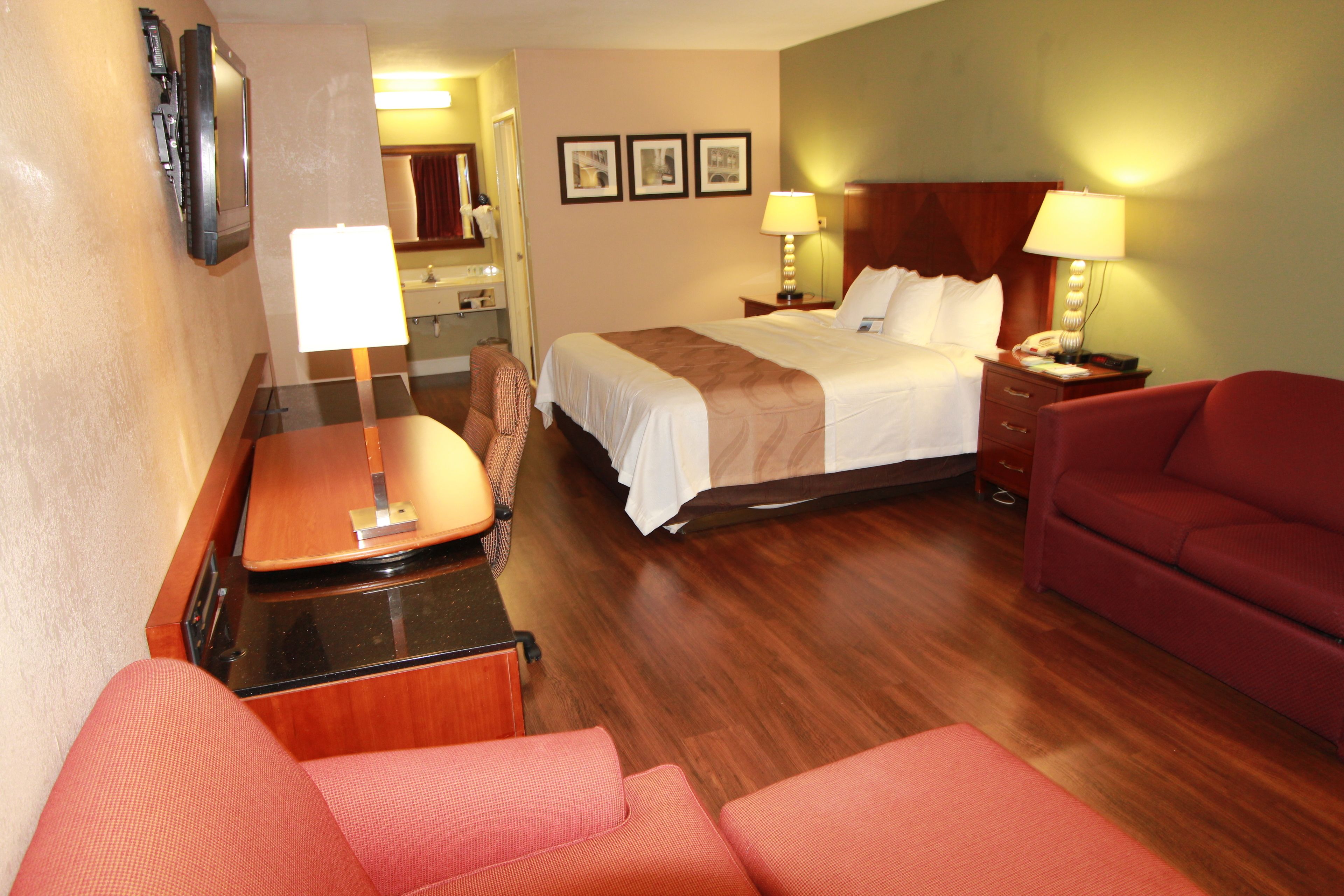 A hotel room with a bed, two bedside tables with lamps, a red sofa, a wooden desk, and a television.