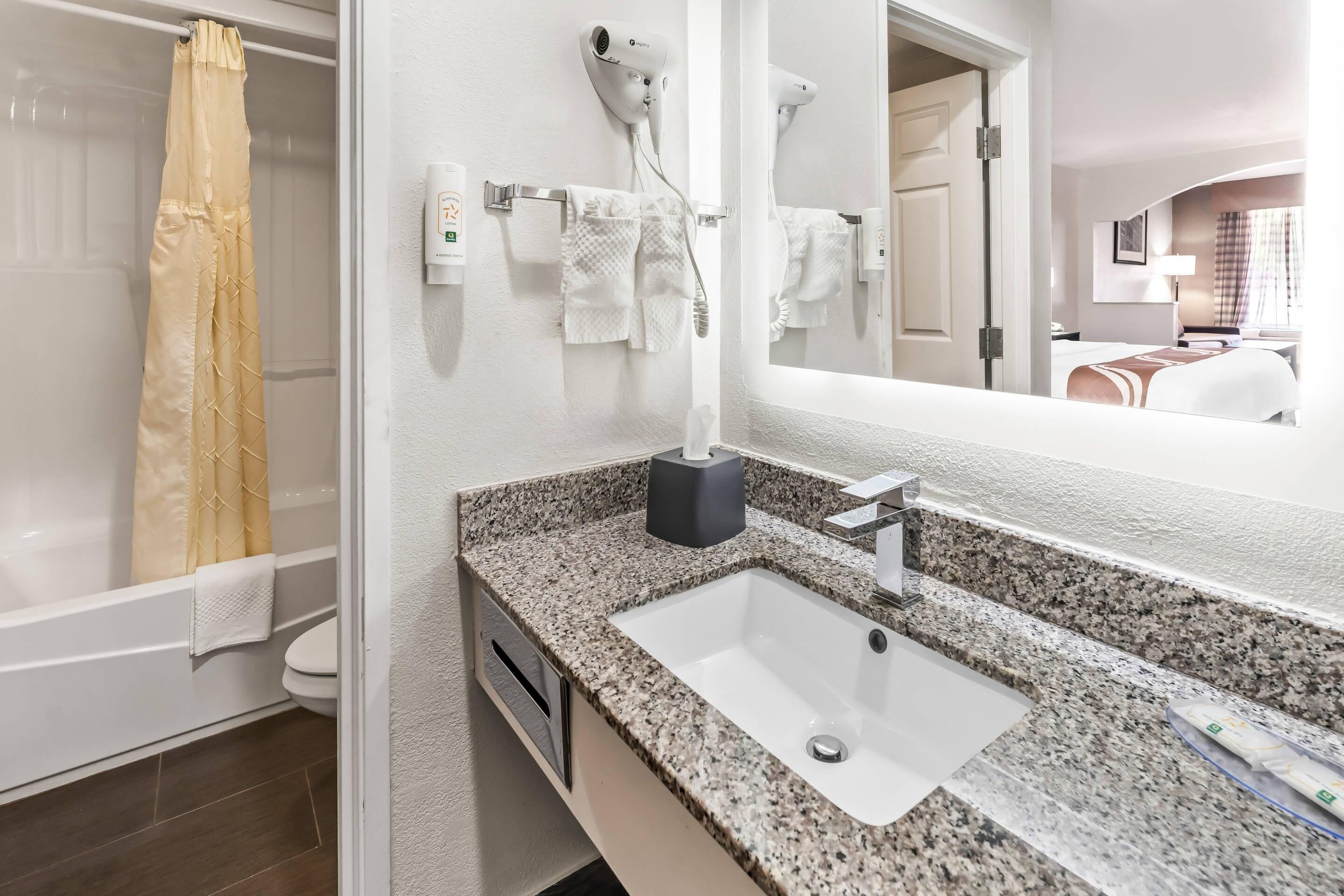 A modern bathroom with a granite countertop sink, a handheld hair dryer, and a shower curtain.