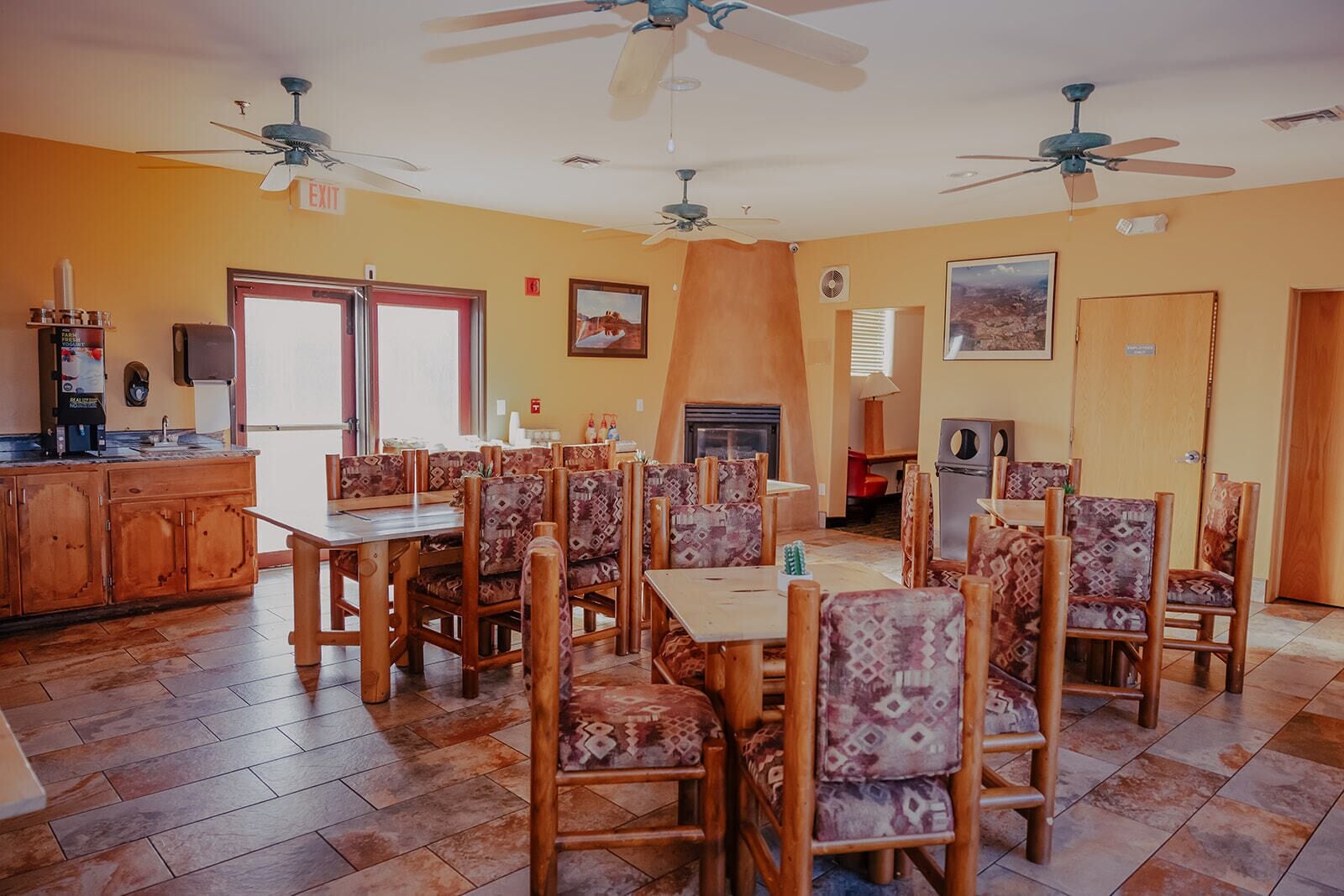 Un espace repas avec des tables et des chaises en bois, une cheminée et des ventilateurs de plafond.