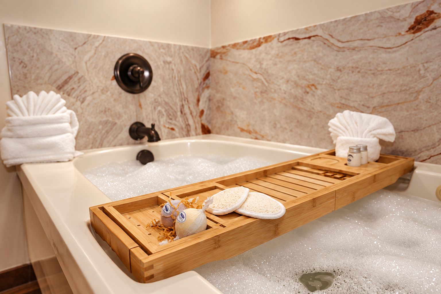 A bathtub with a wooden tray holding bath products, towels, and a bottle of shampoo.
