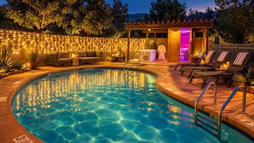 Piscina com área central submersa, rodeada por espreguiçadeiras e um espaço coberto com iluminação de corda.