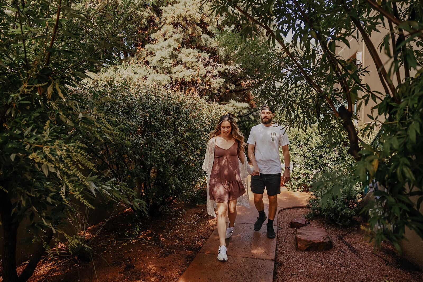 A couple walking on a pathway surrounded by dense foliage and trees.