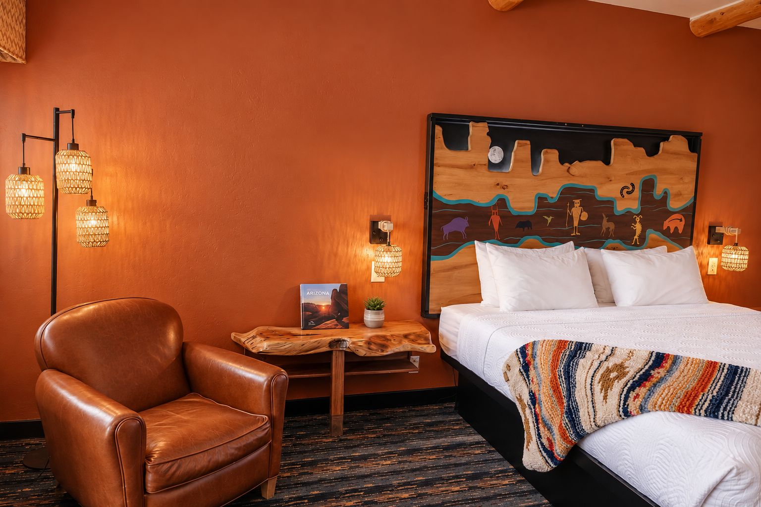 Habitación de hotel con cama, un sillón de cuero, una mesita con un libro y luces en la pared.