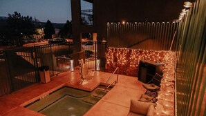 Ett poolområde på taket med en jacuzzi, sittplatser och en stenmur dekorerad med ljusslingor.