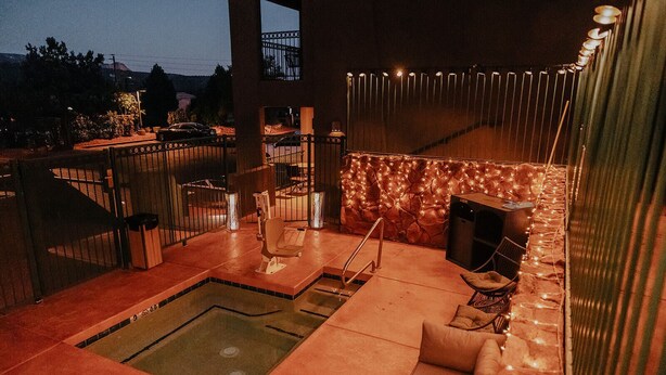 Uma área de piscina no terraço com hidromassagem, assentos e uma parede de pedra com luzes de cordão.