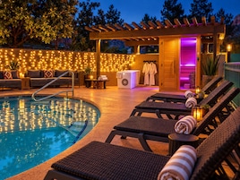 Ein Poolbereich mit Liegestühlen, einem Whirlpool und einer Pergola mit Lichterketten.