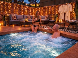 Un jacuzzi con dos personas, rodeado de asientos exteriores y luces colgantes.