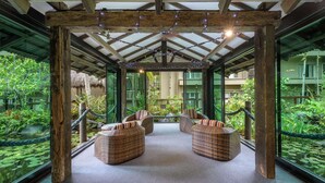 Un espace de détente abrité, doté de mobilier en osier et offrant une vue sur un jardin luxuriant grâce à des murs de verre.