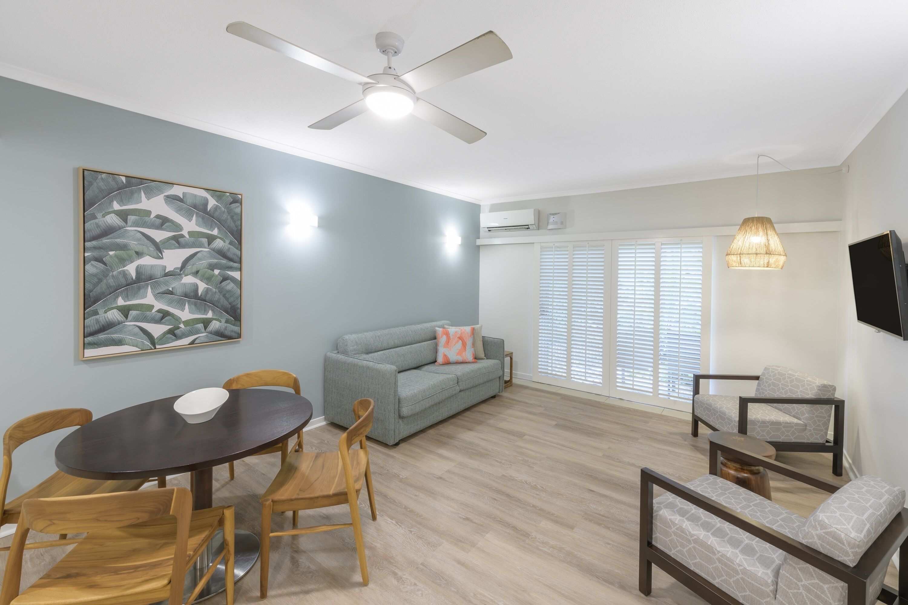 A living room with a dining table, chairs, a sofa, a TV, and a ceiling fan.