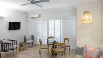A modern living room with a ceiling fan, a dining table with chairs, a sofa, and a TV mounted on the wall.